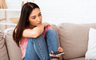 Frustrated woman holding mobile phone sitting on the couch