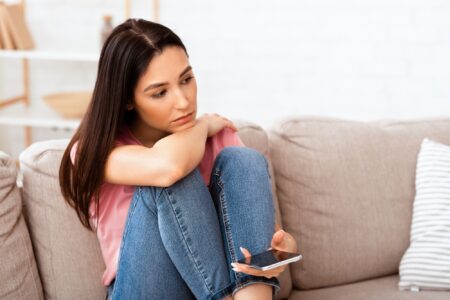 Frustrated woman holding mobile phone sitting on the couch