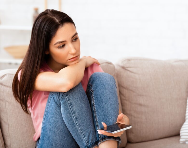Frustrated woman holding mobile phone sitting on the couch