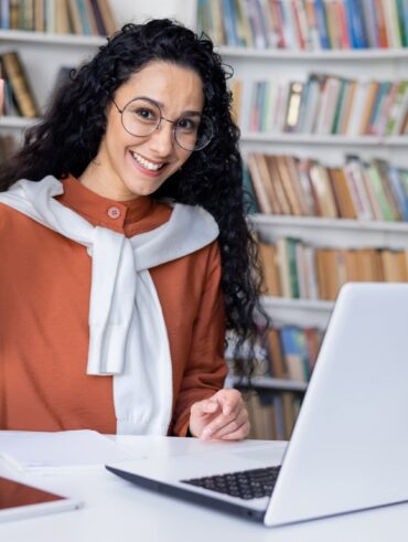 Delighted university student making eureka gesture while sitting by table with pc on background of